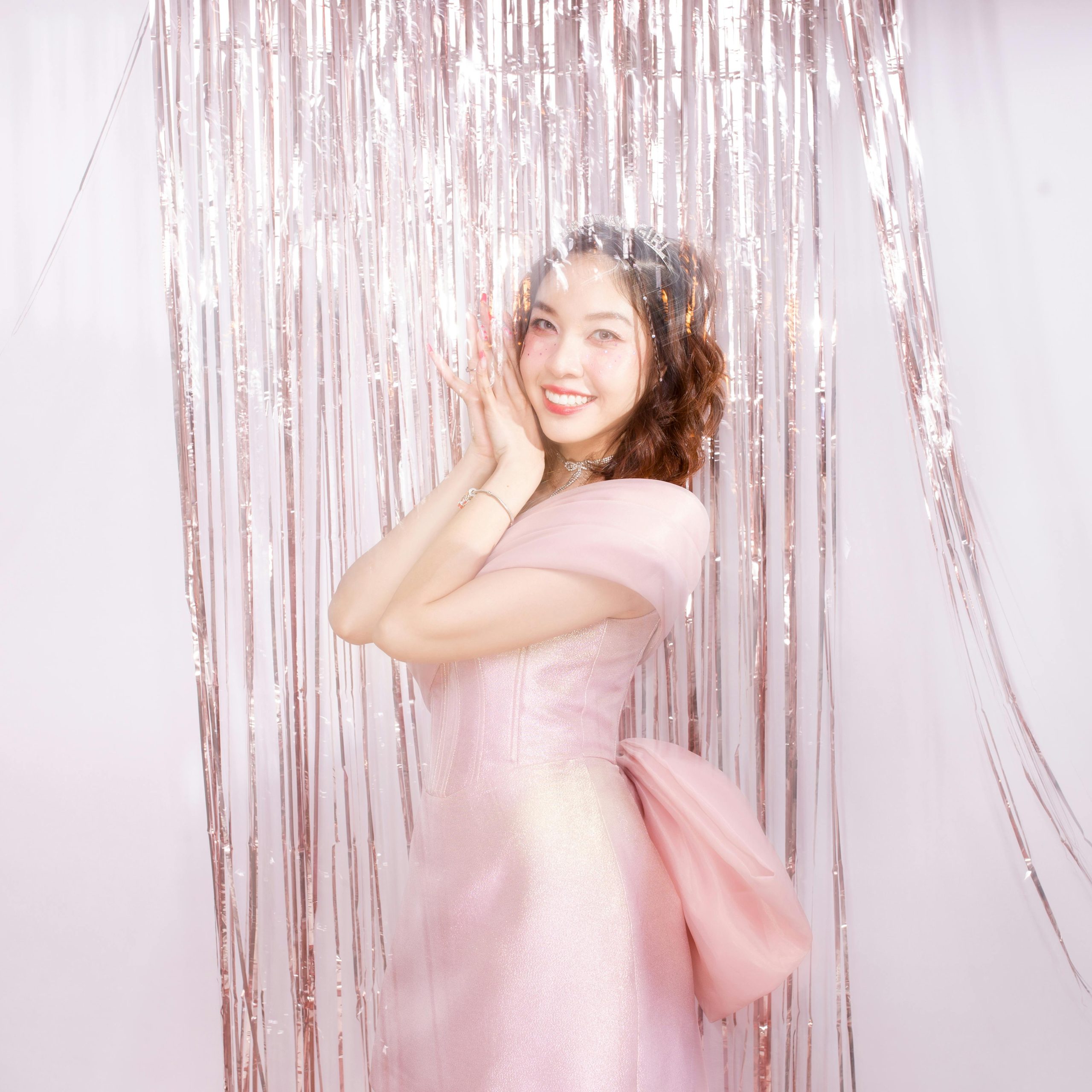 Charming woman in a pink dress posing happily against a festive tinsel backdrop, embodying elegance and joy.